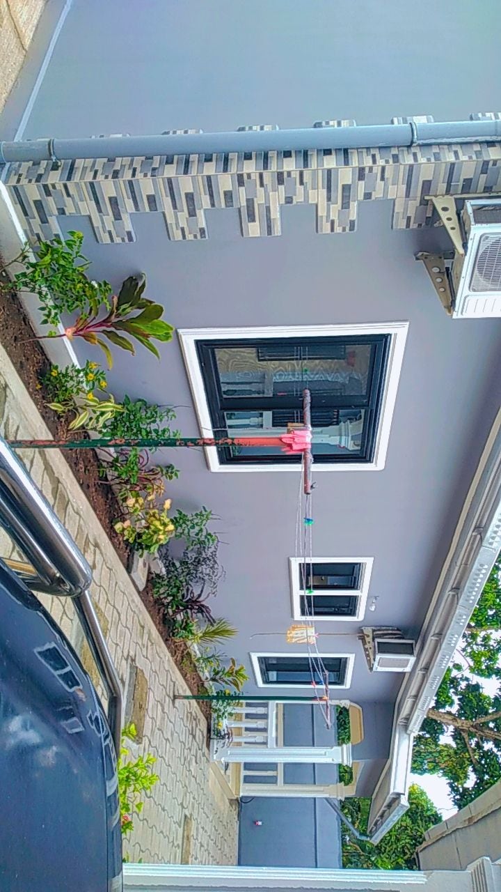 The exterior of the home presents a contemporary design with a gray facade and decorative stone elements. A neatly arranged garden features various plants alongside a stone pathway. A window offers a glimpse into the interior, while outdoor fixtures are also visible.