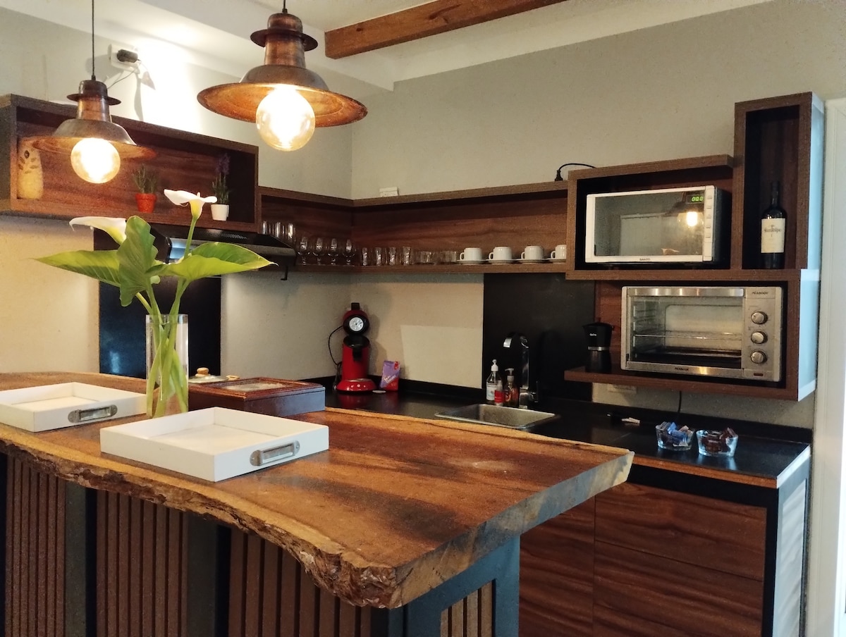 The kitchen is equipped with modern appliances, including a microwave and coffee maker. A wooden countertop adds warmth, complemented by glassware neatly arranged above. Soft lighting is provided by pendant lamps, enhancing the functional design of the space.