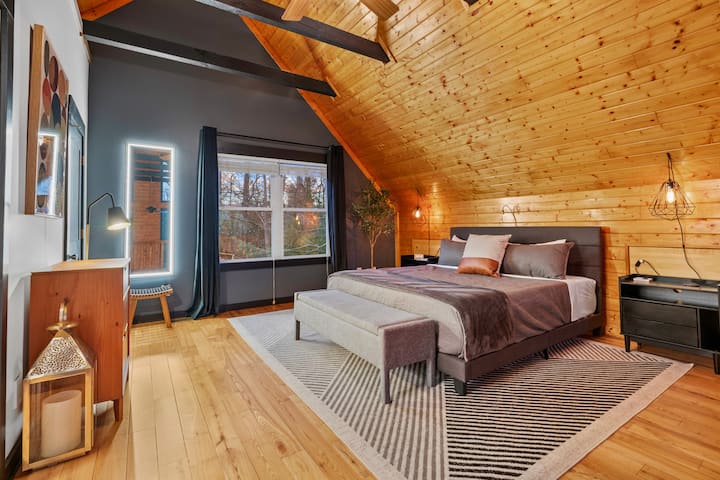 Основната спалня на горния етаж е просторна и предлага достатъчно място за съхранение с скрин, пейка и дрешник. 