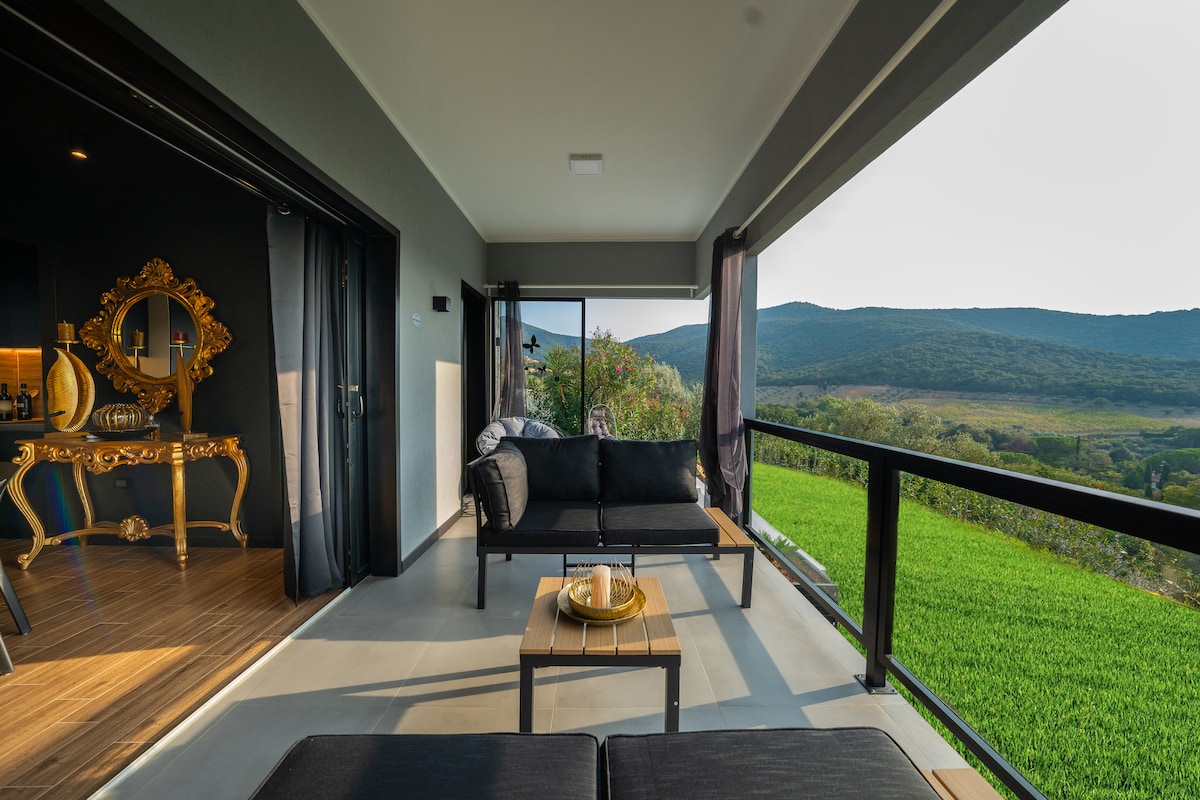 A spacious outdoor terrace features sleek, modern seating arrangements overlooking expansive views of greenery and distant hills. Privacy is provided by flowing curtains, while natural light brightens the area. An elegant table adds a touch of sophistication, inviting relaxation and enjoyment of the surrounding scenery.