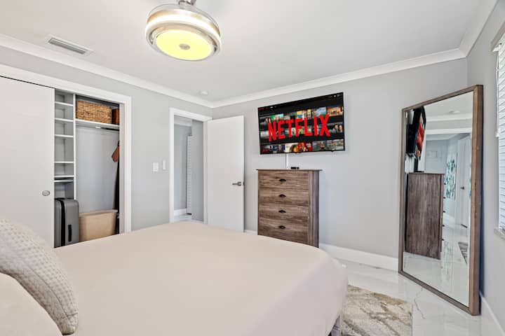 Guest room #1 features a queen sized memory foam mattress, built in storage closet with racks, and shelving, a mounted smart TV, full length mirror, and ambient lighting. 