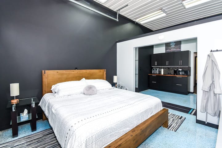 Dormitorio principal con cama tamaño king. Tiene un televisor inteligente de 40pulgadas montado en la pared.  Incluye un ventilador de piso, un despertador y una máquina de sonido para dormir.