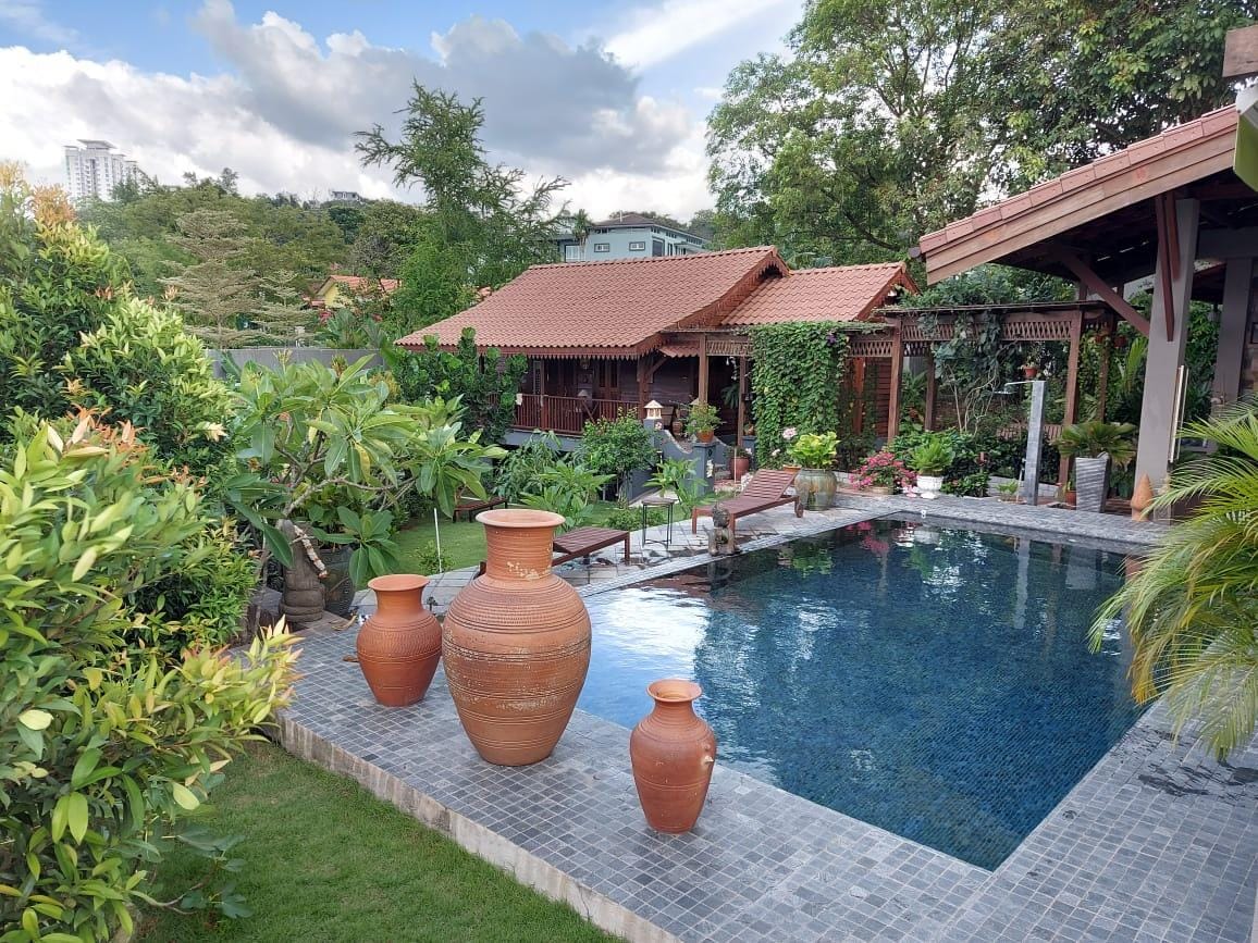 A tranquil swimming pool is framed by lush greenery and decorative planters. Stylish clay pots are placed near the pool, which reflects the surrounding garden. A wooden walkway leads to a chalet, providing easy access to the serene outdoor space.
