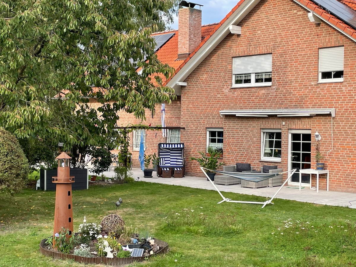 A spacious outdoor area features a well-maintained lawn with ornamental plants and a decorative lighthouse. A hammock and a seating area are visible, complemented by a shaded patio space. The house's brick exterior and large windows invite natural light into the living spaces.