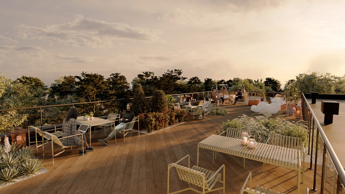 The rooftop terrace features a wooden deck with a variety of seating options, including tables and lounge chairs. Lush greenery and potted plants create a serene environment, while the setting sun casts a warm glow over the space, inviting relaxation and social gatherings.