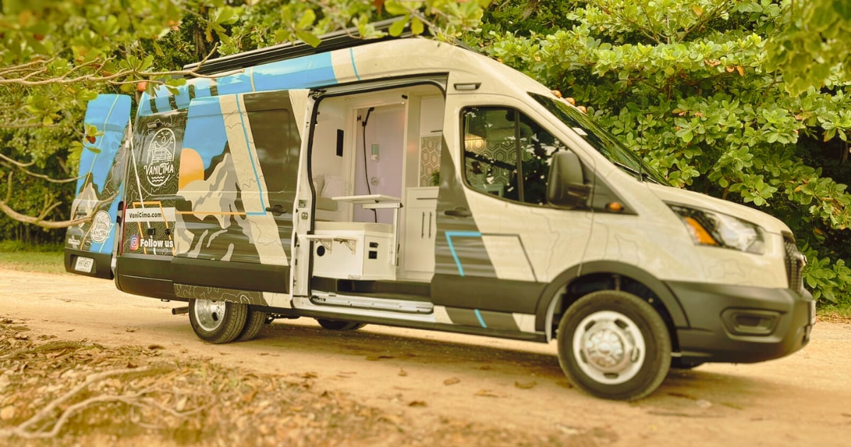 A modern camper van is shown parked amidst greenery, featuring a vibrant blue and graphic design on the side. The sliding door is open, revealing a clean and functional interior layout that includes storage and essential amenities for road travel.