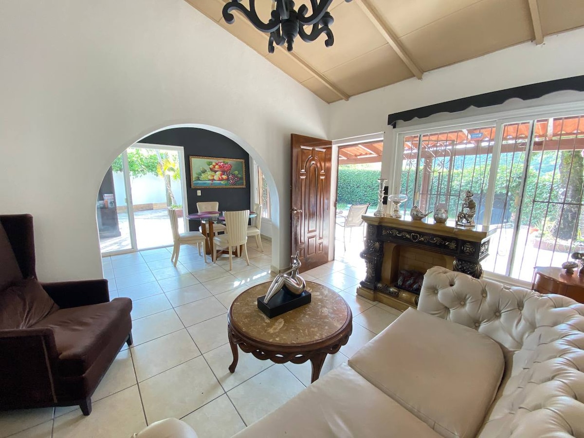 A light-filled living area features a comfortable sofa and a stylish coffee table. An arched doorway leads to a dining area furnished with a set of chairs and a wooden table. Large glass doors open to the outdoor patio, enhancing the space's openness.