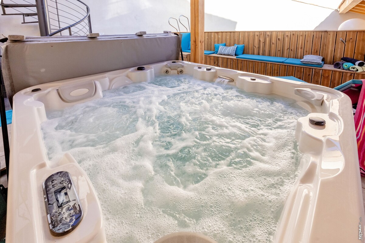 A hot tub with bubbling water is set against a wooden backdrop. Soft seating is arranged nearby, and the area is bathed in natural light, creating a relaxed environment for leisure and enjoyment.