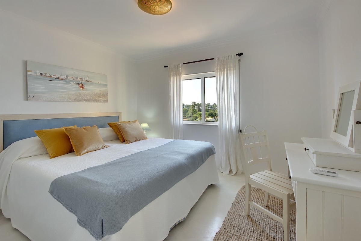 Chambre du milieu avec grand lit, fenêtre avec stores/volets pour une obscurité totale, armoire ouverte, dressing, chaise et miroir, climatisation (chaud/froid) et accès à la salle d'eau avec douche à l'italienne, toilettes et lavabo avec vasque et miroir