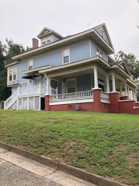 A two-story blue house is situated on a hillside, featuring white trim and a welcoming front porch. The lawn is neatly maintained, and the exterior showcases a blend of brick and siding. A set of stairs leads to the side entrance, enhancing accessibility.