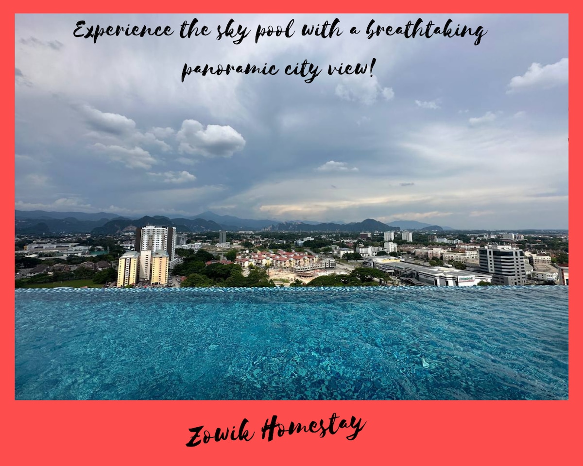 An infinity pool is shown reflecting the skyline, with buildings and green hills visible in the distance. The water's surface merges with the horizon, offering a seamless view of the cityscape under a cloud-filled sky.