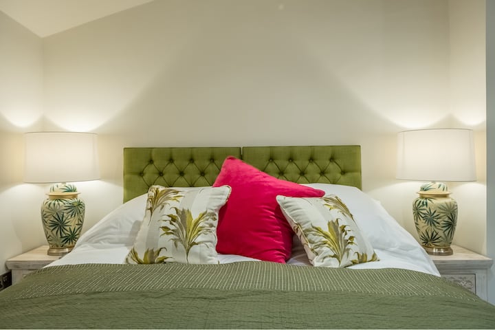 Dormitorio Dos con una cama tamaño king hecha a medida y un colchón con sábanas blancas frescas.  Esta cama se puede convertir en individual. Cajonera, hangares en ganchos para la ropa y televisión inteligente y vistas al patio.