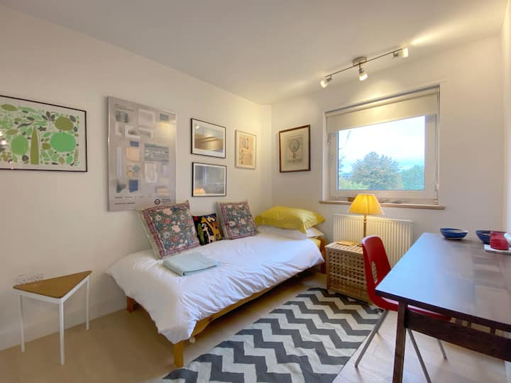 חדר שינה יחיד נדיב, עם שולחן כתיבה אגוזים, הרבה יצירות אמנות על הקירות ושפע של מקום בארון.