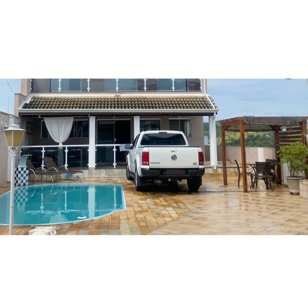 A tranquil outdoor area features a shimmering pool framed by tiled flooring. A white vehicle is parked nearby, with lounge chairs positioned alongside the pool. A pergola provides shaded seating for relaxation, and large glass doors lead to the inviting interior of the home.