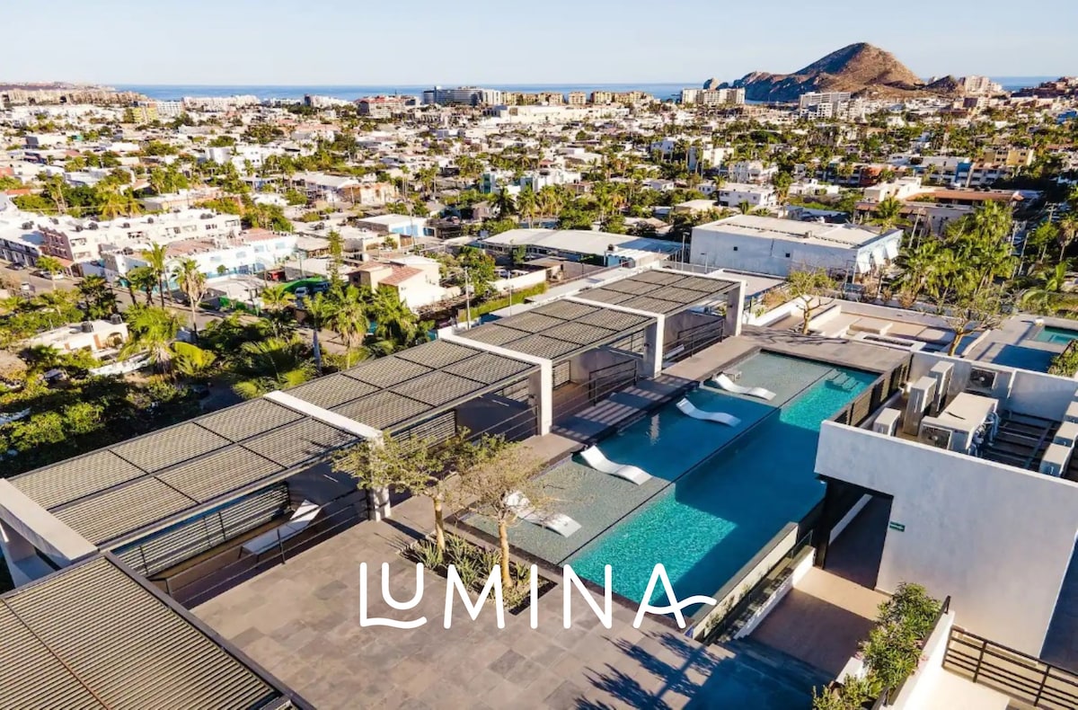 An aerial view of the rooftop terrace reveals a spacious pool and lounge area surrounded by minimalist landscaping. The layout showcases shaded seating areas with views of the surrounding city and mountains, highlighting the outdoor leisure space available for relaxation.