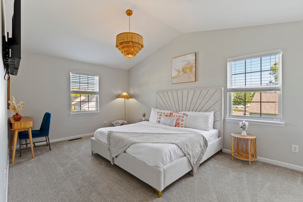 Spacious master bedroom with a luxurious king-sized bed, adorned with soft linens and decorative pillows. Natural light fills the room, creating a bright and relaxing atmosphere.
