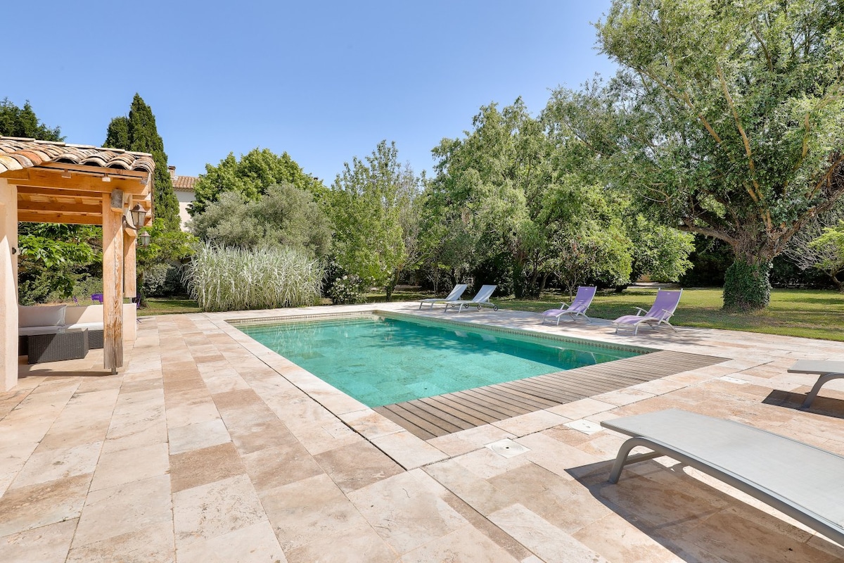 A private pool area showcases a clear, inviting water surface surrounded by a tiled deck. Sun loungers are arranged along one side, nestled amongst greenery including shrubs and trees. The tranquil setting offers a serene escape within the expansive park.