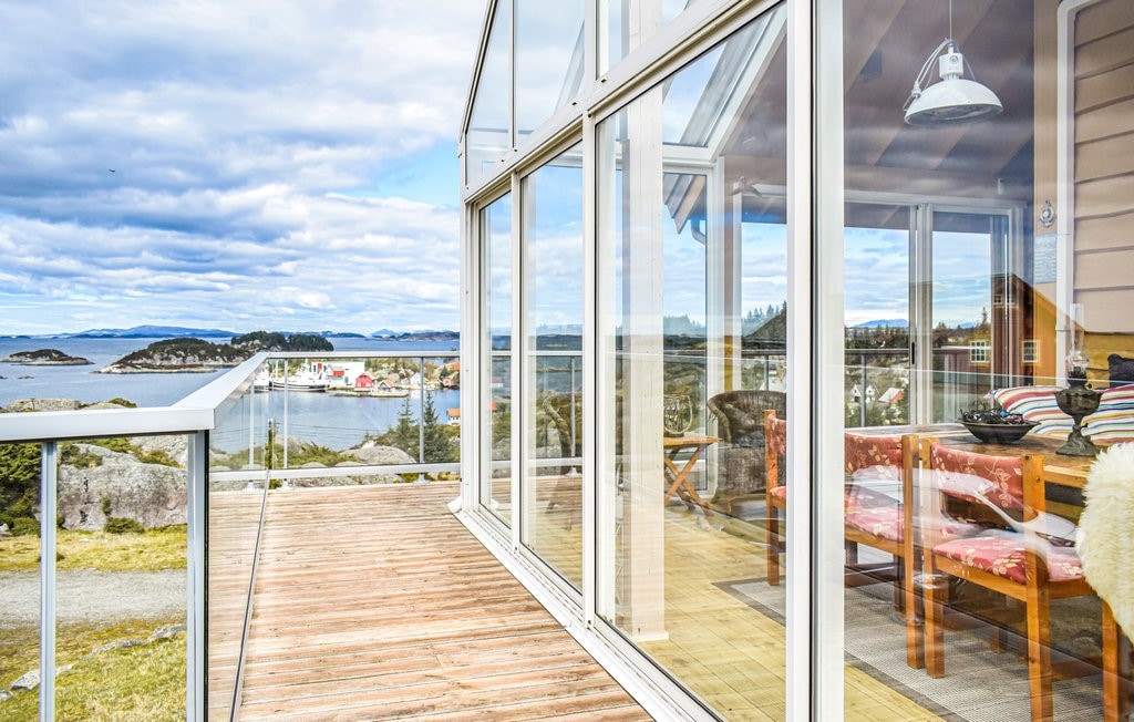A large winter garden is featured with expansive glass walls, providing unobstructed views of the surrounding landscape. A wooden deck extends into the outdoor space, and comfortable seating is arranged inside, offering a bright and airy atmosphere.
