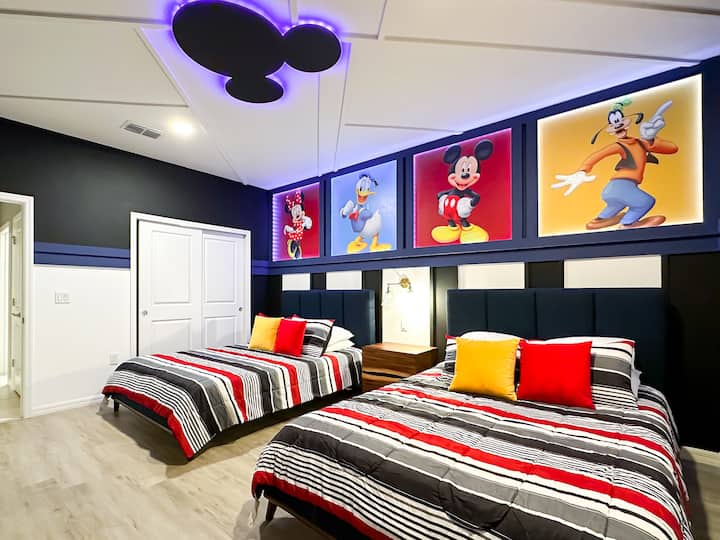 Tritt ein in diese moderne Disney-Traumhöhle! Die Plattformbetten sind mit gestreiften Steppdecken und kräftigen rot-gelben Akzenten ausgestattet. Oben zeigen beleuchtete Tafeln Minnie, Donald, Mickey und Goofy. Elegante schwarz-weiße Streifen, eine leuchtende Mickey-Silhouette