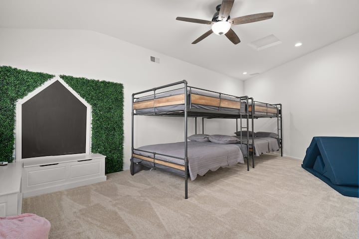 Chumba hiki kikubwa cha kulala, kinachochukuliwa kuwa "chumba cha watoto" kina dari zilizopambwa na vitanda viwili vya ghorofa vya Queen-Over-Queen pamoja na kochi la kawaida la kuchezea na ukuta wa kifahari