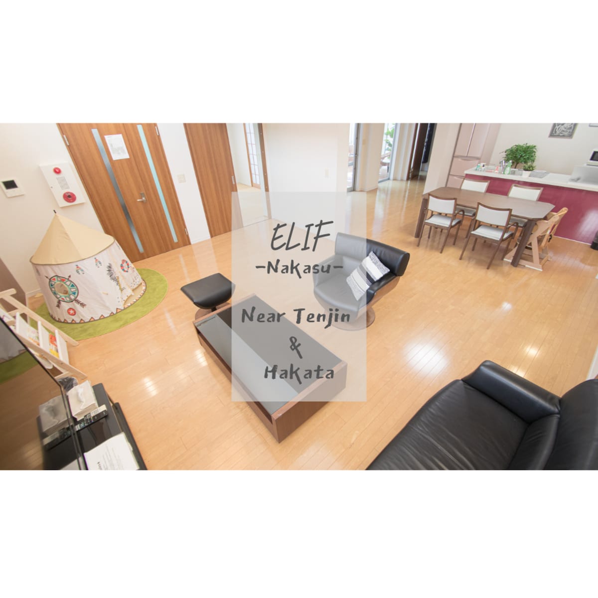 A spacious living area features a comfortable black couch and a round coffee table. A play tent is present in the corner, while a dining table with several chairs is positioned nearby. Natural light fills the space, enhancing its welcoming layout.
