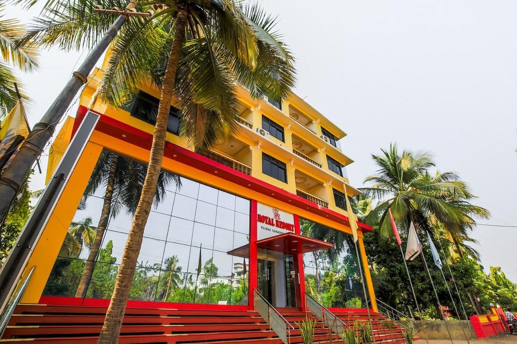 The resort's exterior is characterized by a vibrant façade, featuring large glass windows that reflect the surrounding greenery. Palm trees frame the building, enhancing its tropical appearance. The entrance is emphasized by a welcoming pathway leading to the lobby.