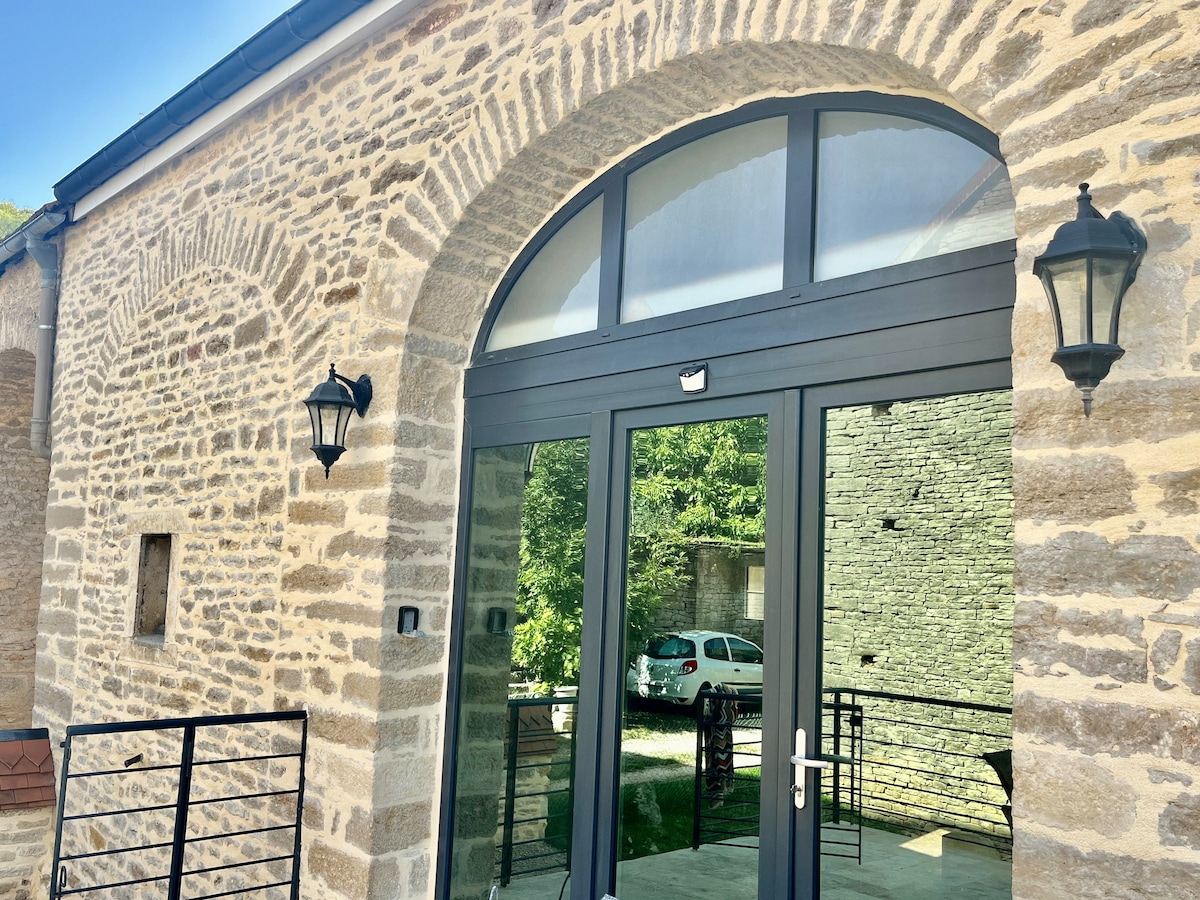 The entrance showcases a large glass door framed by an arch, set within a rustic stone facade. Stylish outdoor lights are positioned on either side of the door, and the reflection of the surrounding greenery can be seen in the glass.