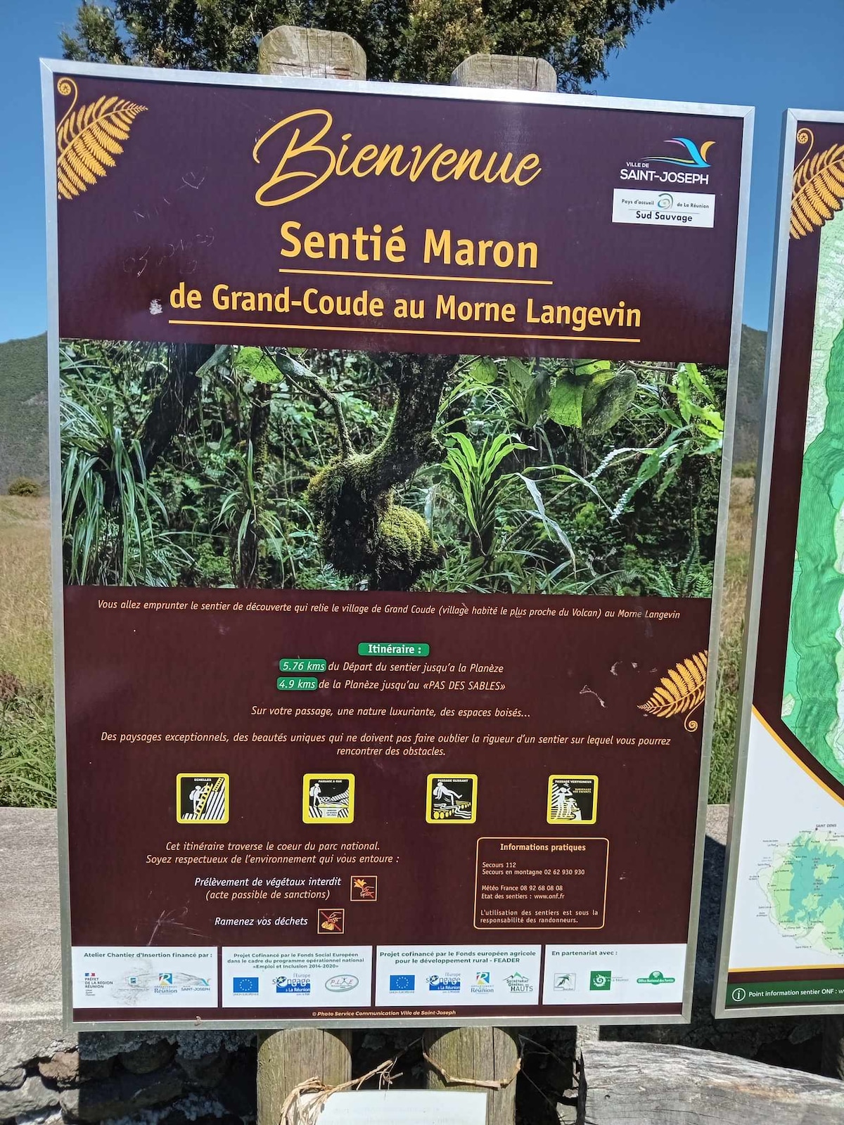 A sign providing welcome information about the Sentier Maron trail, which stretches from Grand Coude to Morne Langevin. The sign features descriptive visuals of the trail and its surroundings, including local wildlife and plant life, along with maps indicating points of interest.