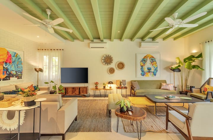 ✨This vibrant living space blends tropical freshness with artistic charm — pops of color, natural textures, and mid-century furniture sit under pastel green beams, creating a stylish, easygoing sanctuary✨