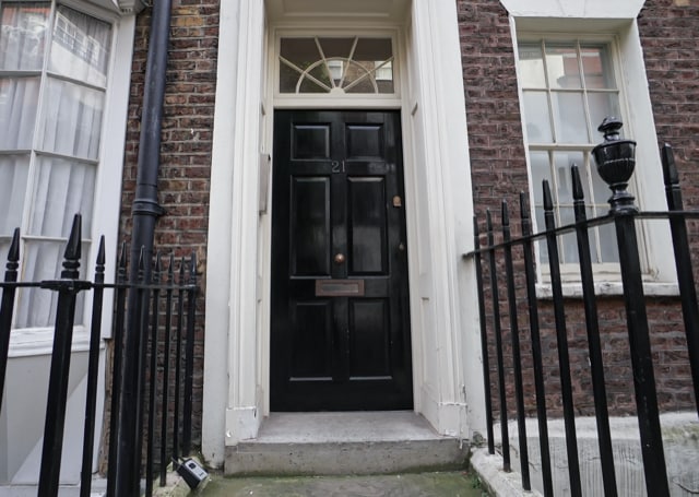 The entrance to the flat features a classic black door set within a brick facade. A decorative wrought iron railing surrounds the entrance, providing a sense of defined space. Large windows on either side allow natural light to enhance the exterior.