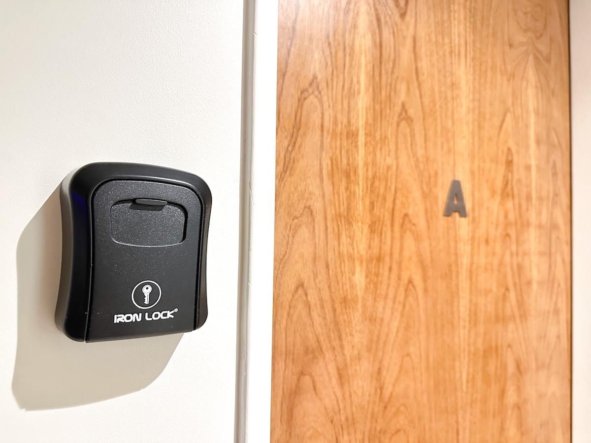 A secure key lockbox is mounted beside a wooden door, featuring a clear letter 'A' identifier. The soft lighting highlights the door's grain texture, emphasizing the simplicity of the entryway.