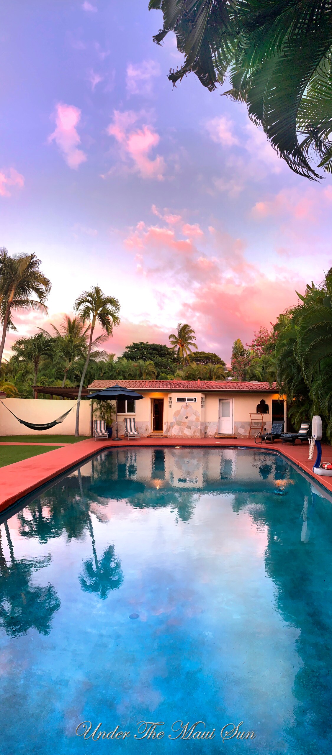 A serene saline pool reflects the pastel colors of the sky, surrounded by lush palm trees. A cozy hammock can be seen nearby, and the villa's charming exterior is visible in the background, blending with the tropical landscape.