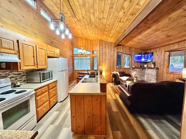 A modern kitchen area with wooden cabinetry and a seamless countertop extends into a cozy living room. Large windows allow natural light to illuminate the space, highlighting a comfortable seating arrangement and a television mounted on a brick accent wall.