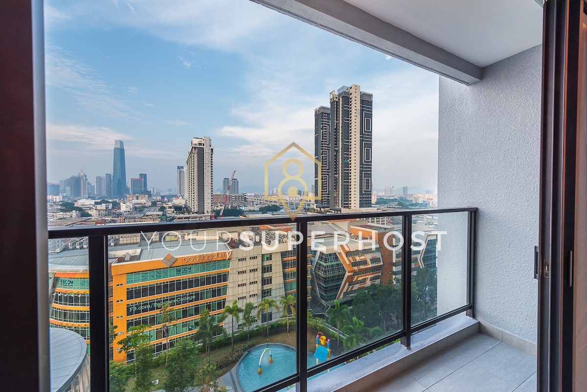 A balcony view overlooks the vibrant Kuala Lumpur cityscape, showcasing a mix of modern skyscrapers and green spaces below. The glass railing enhances the open feel, allowing for unobstructed views of the skyline against a backdrop of blue sky and scattered clouds.