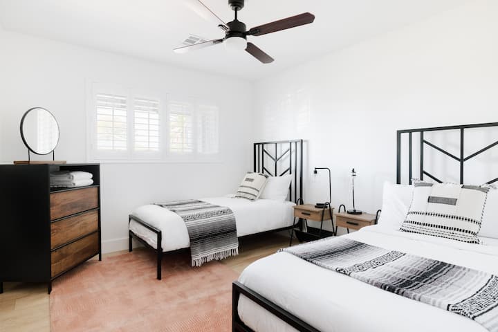 Bright and cozy twin bedroom featuring two comfortable beds, a ceiling fan, full-length mirror, dresser, and closet — perfect for friends, kids, or guests sharing space during your Scottsdale stay.