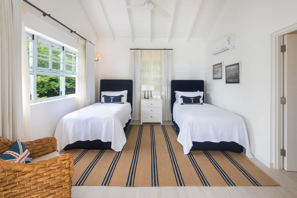 Dos camas individuales a juego en un amplio dormitorio con baño y vistas al mar.