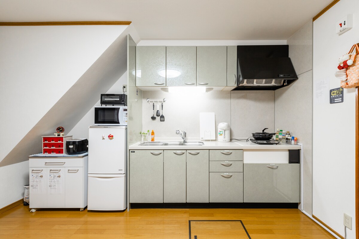 The kitchen features modern appliances including a refrigerator, microwave, and stovetop. Light-colored cabinetry provides ample storage space, while a kitchen sink sits beneath a bright ceiling light. Counter space is available for meal preparation, ensuring convenience for cooking needs.