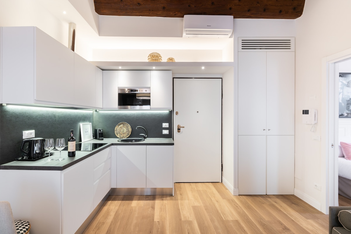 A modern kitchen area is equipped with sleek cabinetry and stainless-steel appliances. The minimalist design features a black countertop with a stovetop and microwave. A small dining space is visible, creating an inviting area for meals.