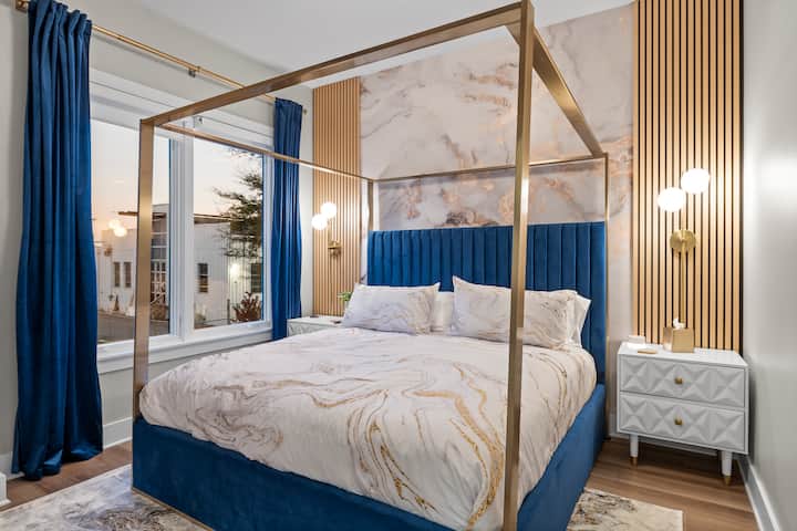 Изискана спалня с луксозно двойно легло с балдахин, с зашеметяваща мраморна акцентна стена и плюшена кадифена табла