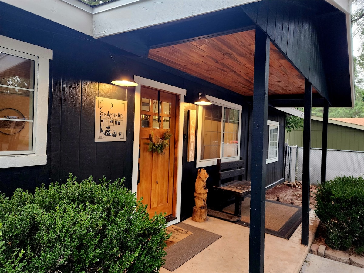 The entrance features a welcoming black and white facade, highlighted by a rustic wooden door adorned with a seasonal wreath. Surrounding greenery adds a natural touch, and a covered porch offers a space to relax before stepping inside.