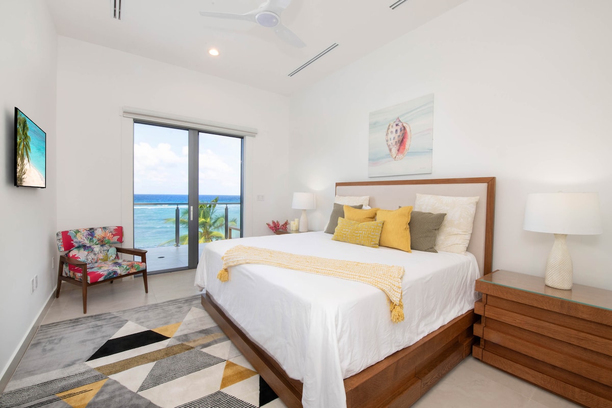 Quarto 5 com cama king size, TV HD e acesso à varanda com vista para o mar.