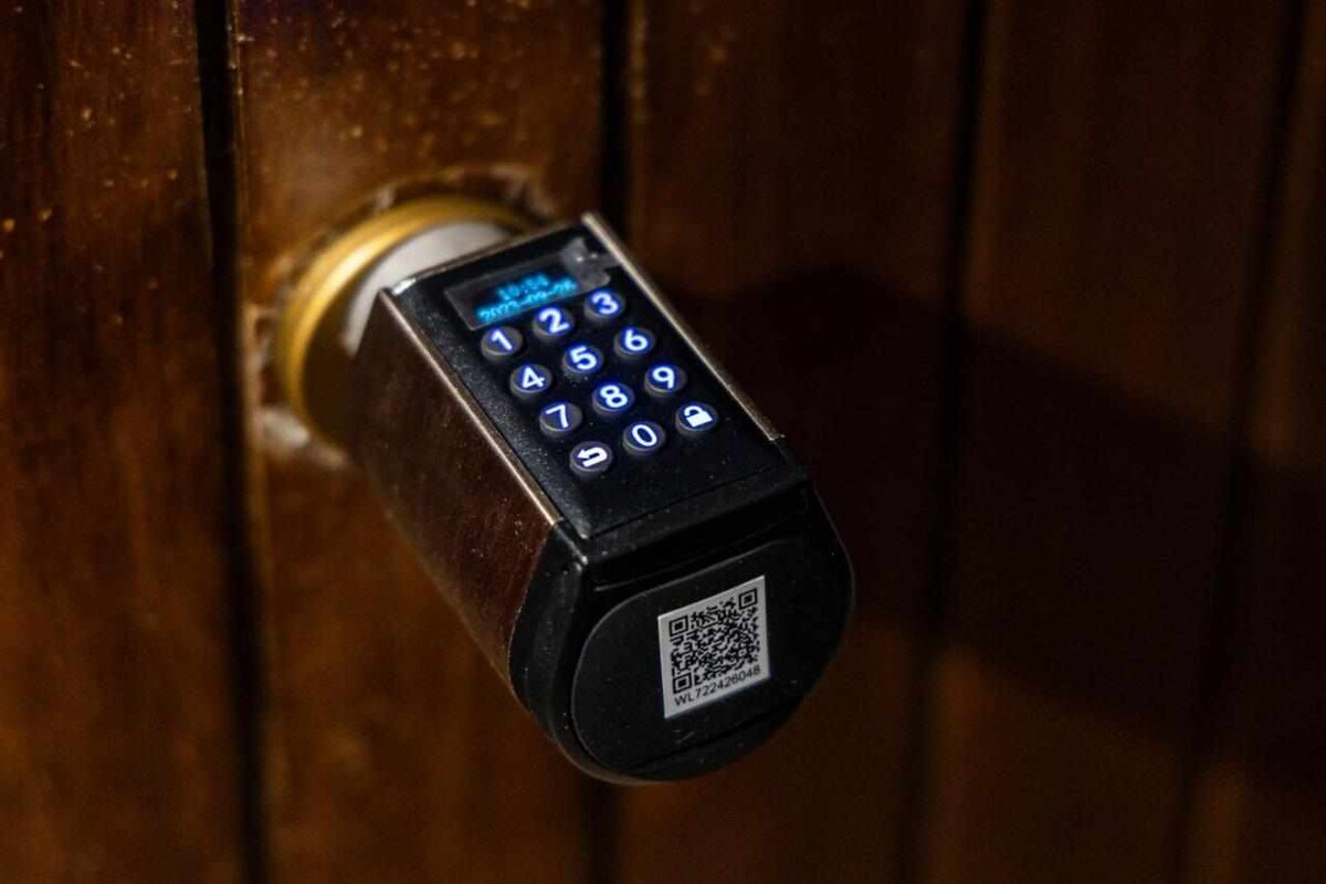 A digital keypad lock is shown on a wooden door, featuring numbered buttons and a QR code. The lock’s design offers a modern touch, ensuring secure self-check-in access for guests.