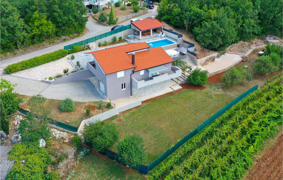 An aerial view captures a modern vacation home surrounded by greenery, complemented by a private pool and covered terrace. The property features a spacious yard with well-defined landscaping and is bordered by a vineyard, creating a serene countryside ambiance.