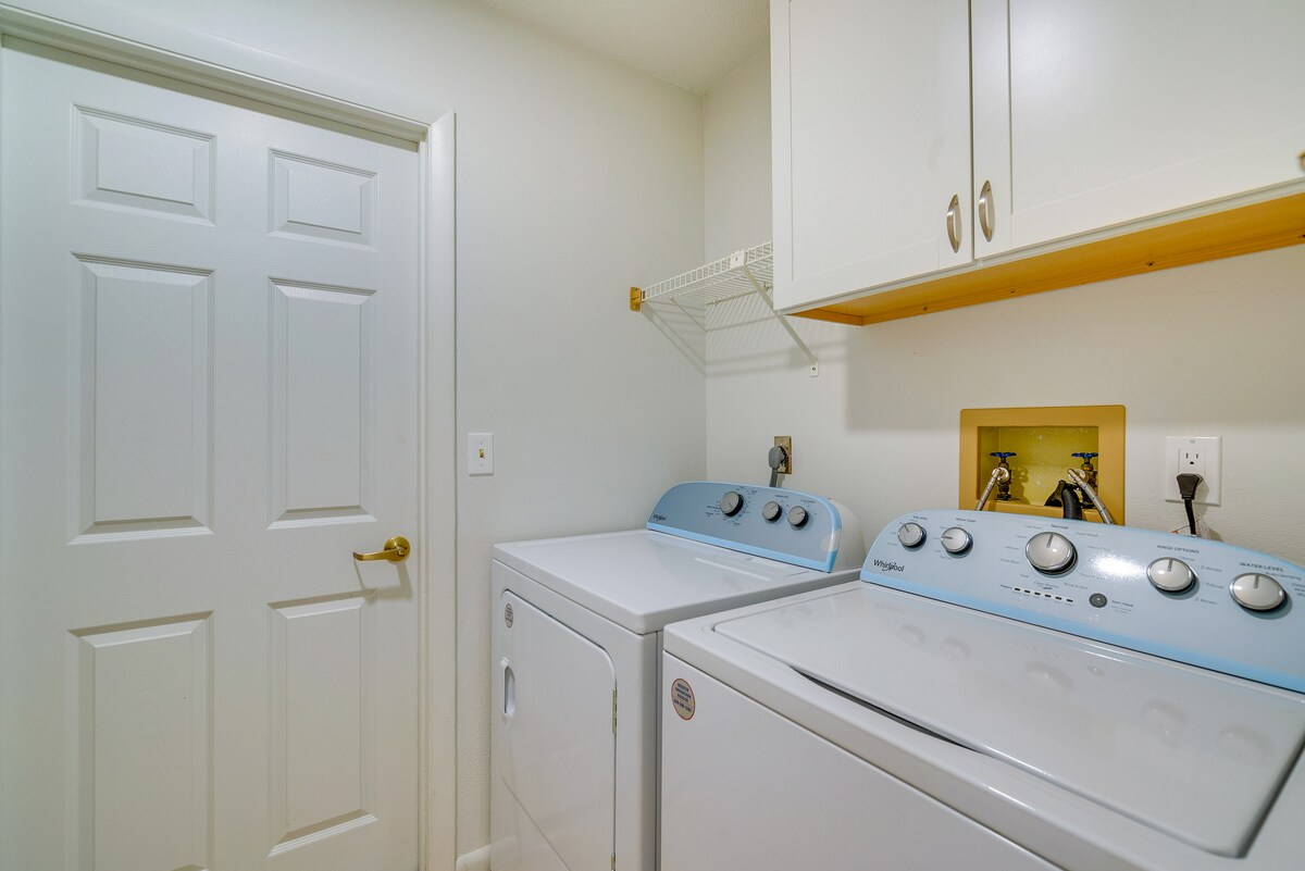 The laundry area features a washing machine and dryer in light blue tones. Above the appliances, a shelf provides additional storage. A white door leads to another space, while neutral-colored walls create an airy feel.