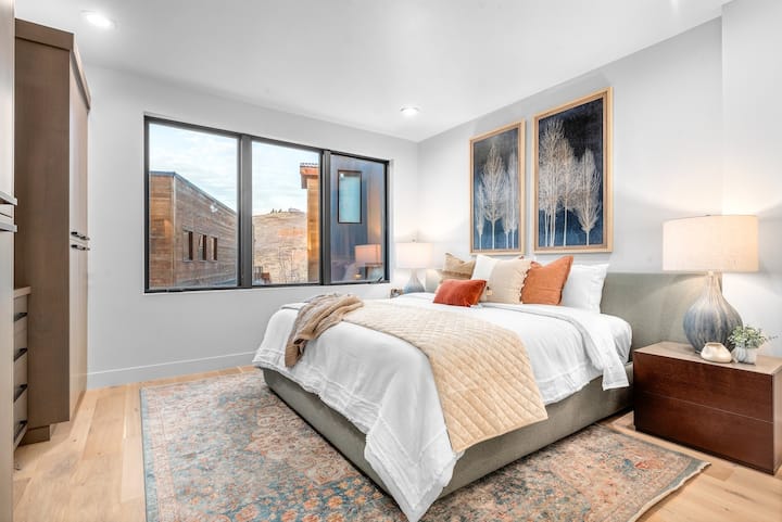 ห้องนอนใหญ่มีเตียงคิงไซส์ หน้าต่างบานใหญ่ที่มีแสงธรรมชาติเข้ามาเยอะ งานศิลปะที่ทันสมัย และตู้เสื้อผ้าขนาดใหญ่