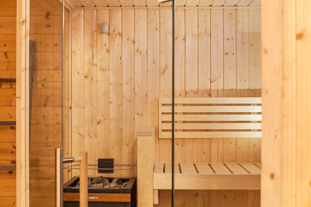 A serene Finnish sauna is presented with natural wood paneling, featuring a wooden bench and a stone heater. The glass door provides a view into the calming space, inviting guests to relax in a soothing environment.