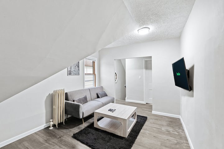 Hapësirë ndenjjeje e rehatshme dhe elegante me një divan gri modern, tavolinë kafeje elegante dhe televizor inteligjent të montuar, i përsosur për t 'u çlodhur.