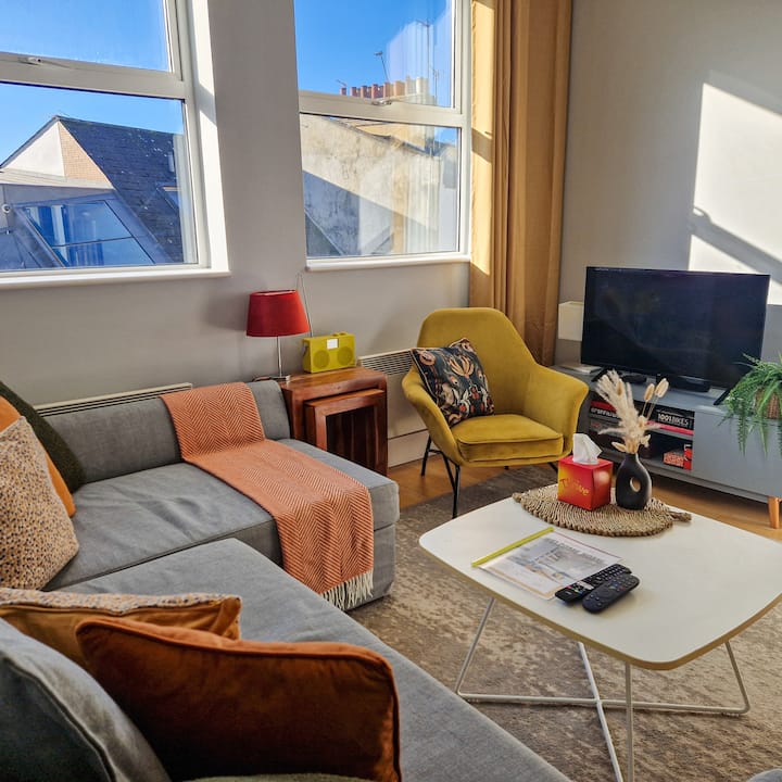 Bright, cozy living space with a comfy sofa, stylish armchair, smart TV, and warm décor. A relaxing spot to unwind, work, or enjoy longer stays with plenty of natural light.
