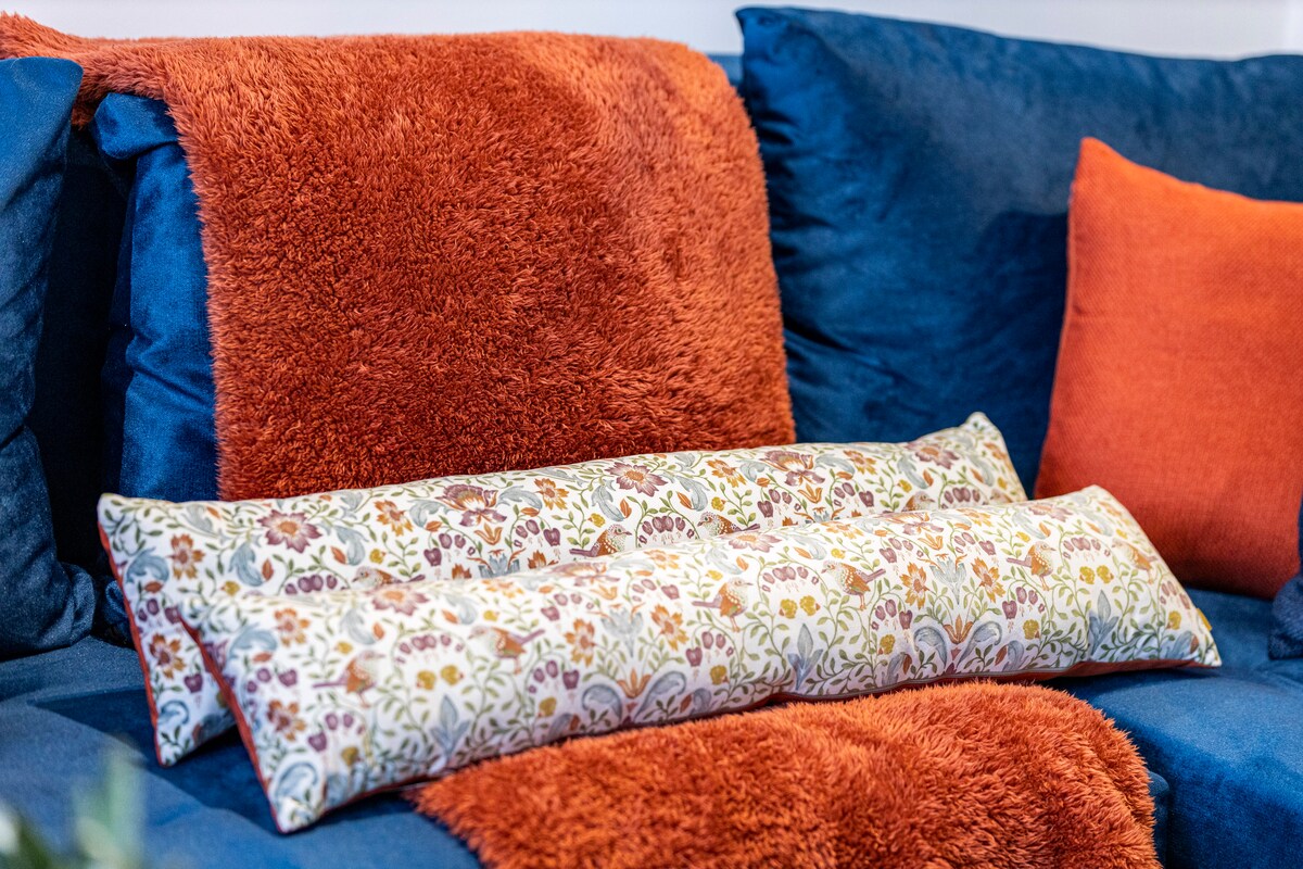 - Divan i gjallë me jastëk të rehatshëm dhe jastëk me lule  
- Ngjyrat e guximshme portokalli dhe blu ndriçojnë ambientin e ndenjjes  
- Dekori elegant i banesave në Airbnb krijon një atmosferë të ngrohtë  
