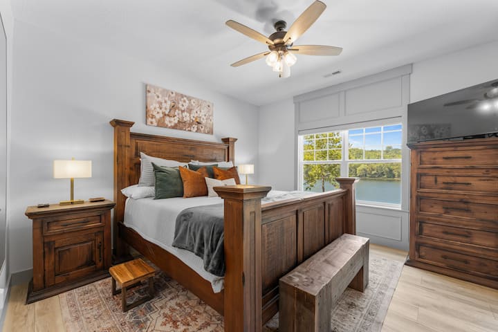 Relax in this cozy bedroom featuring rustic wooden furnishings and a stunning lake view visible from the large window.